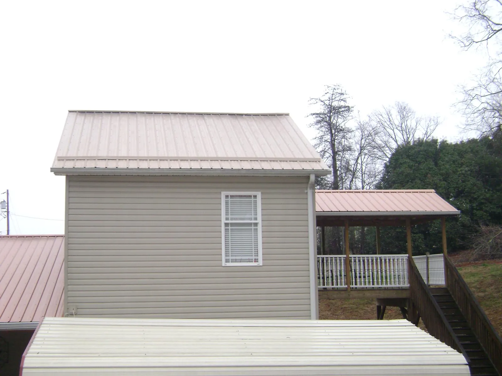 Tan metal roofs on a two story addition and attached porch, from a Roof Replacement job in Jamestown
